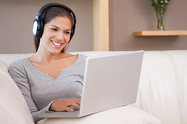 Woman on Couch Wearing Over-the-Ear Headphones Using Laptop